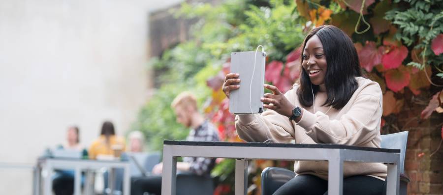 A student using a tablet in the Camper Coffee courtyard outside Queen's Building 