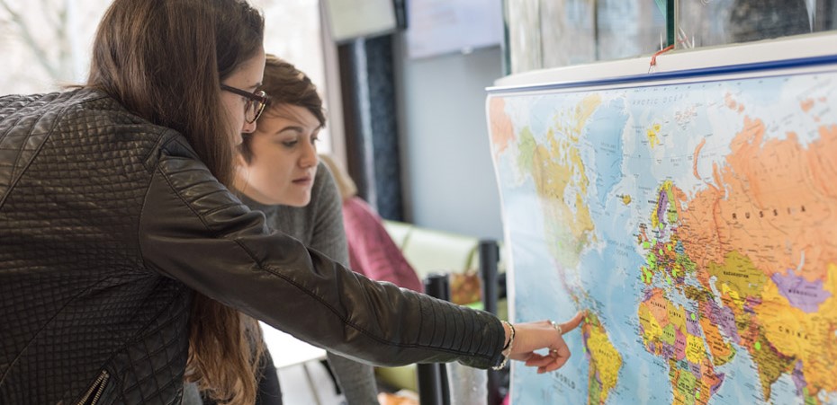 two students pointing at a map of the world