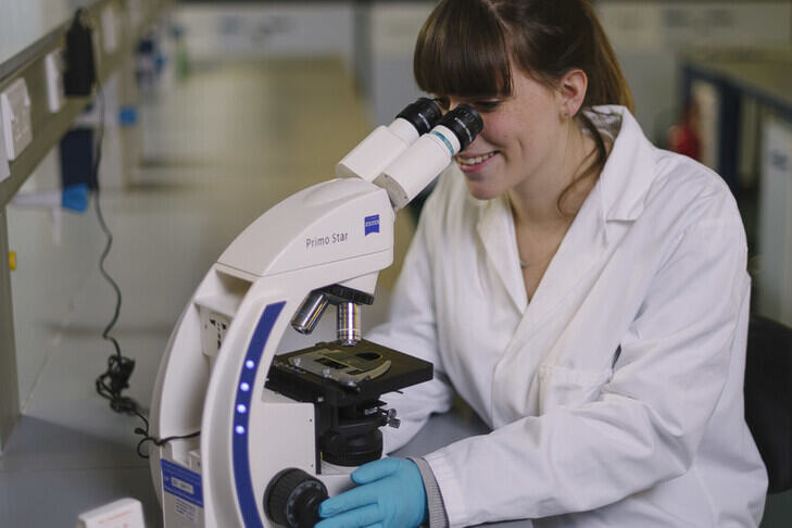 Woman in lab coat studying microscope