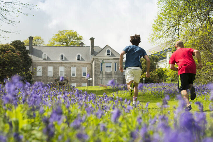 Two students jogging between the bluebells, towards Tremough House.