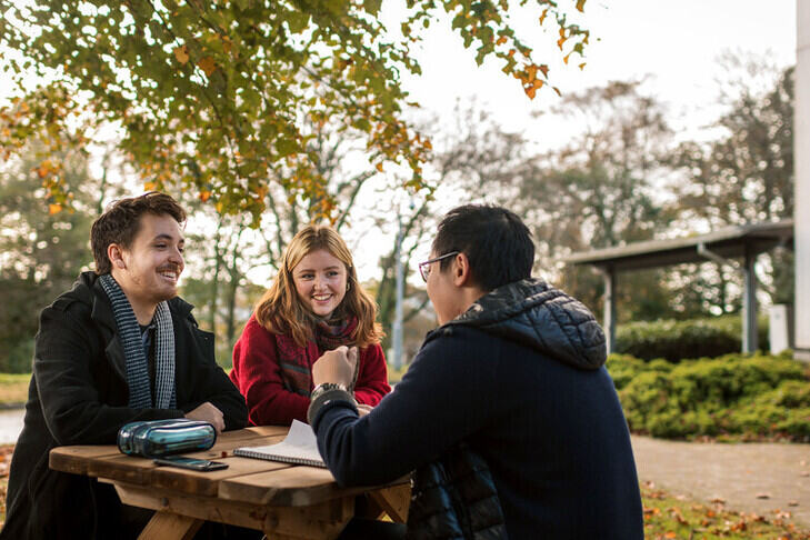 Students sat at a picnic bench in autumn.