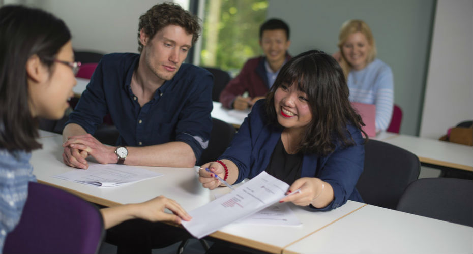 Students sitting at desks discussing content on a piece of paper