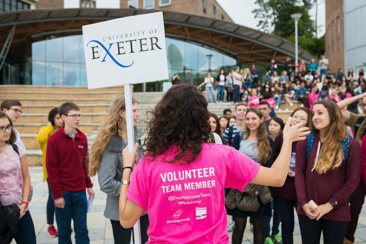 A volunteer wearing a pink t-shirt and holding a University of Exeter sign 